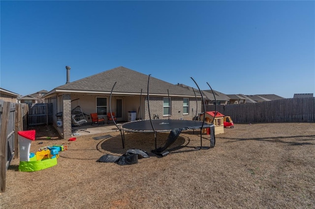 rear view of house featuring a patio, a trampoline, roof with shingles, and a fenced backyard