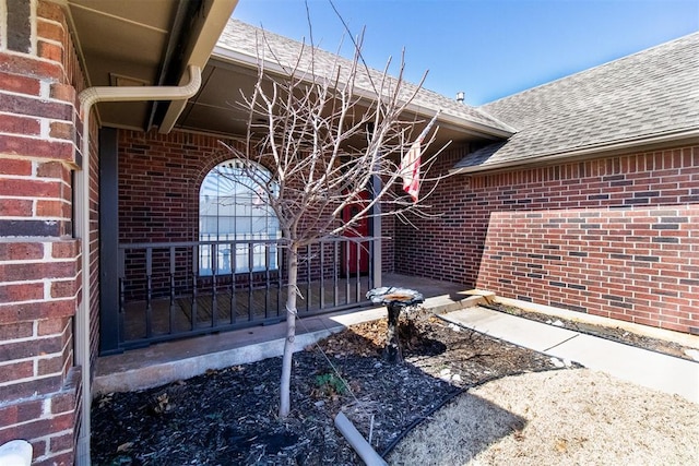 view of exterior entry with brick siding and a shingled roof