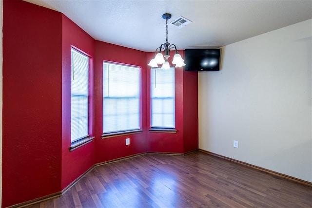 empty room featuring a notable chandelier, baseboards, visible vents, and wood finished floors