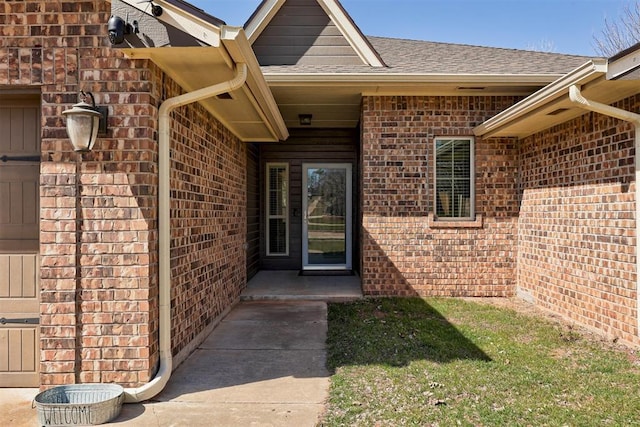 doorway to property featuring brick siding and roof with shingles