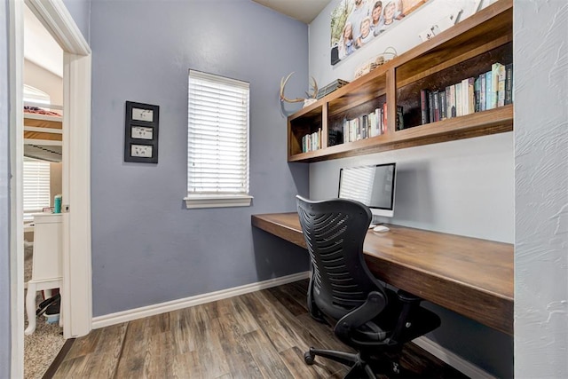 office featuring baseboards, built in desk, and wood finished floors