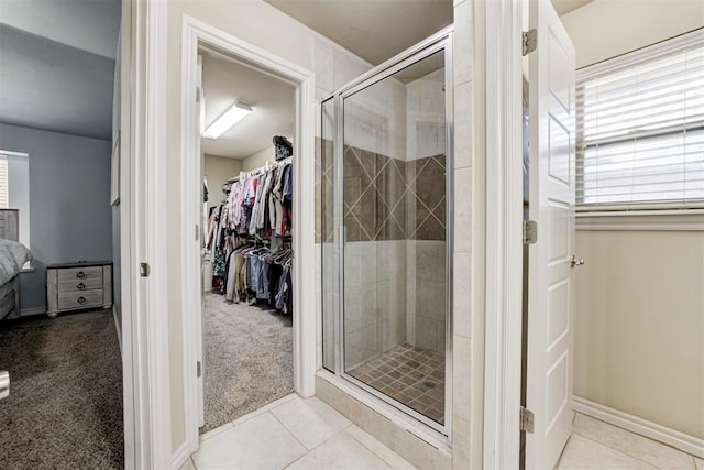 ensuite bathroom featuring baseboards, a spacious closet, tile patterned flooring, and a stall shower