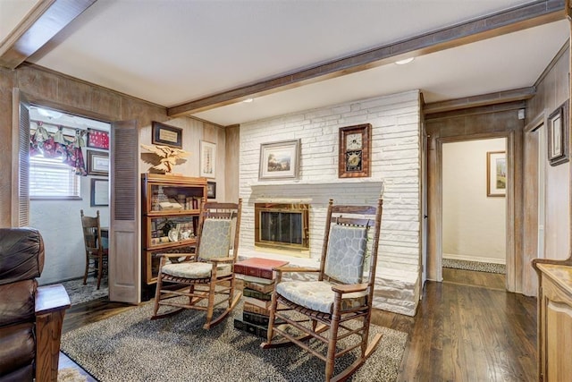 dining area featuring beam ceiling, wood walls, a brick fireplace, and dark wood-type flooring