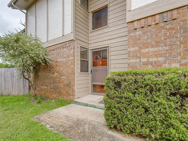 entrance to property featuring brick siding and fence