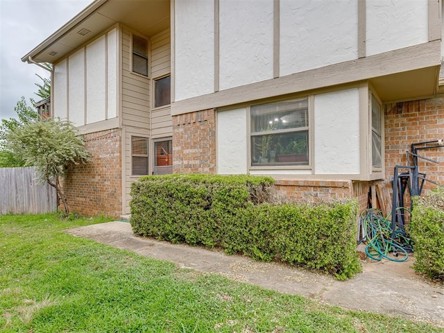 view of property exterior with stucco siding, fence, brick siding, and a lawn