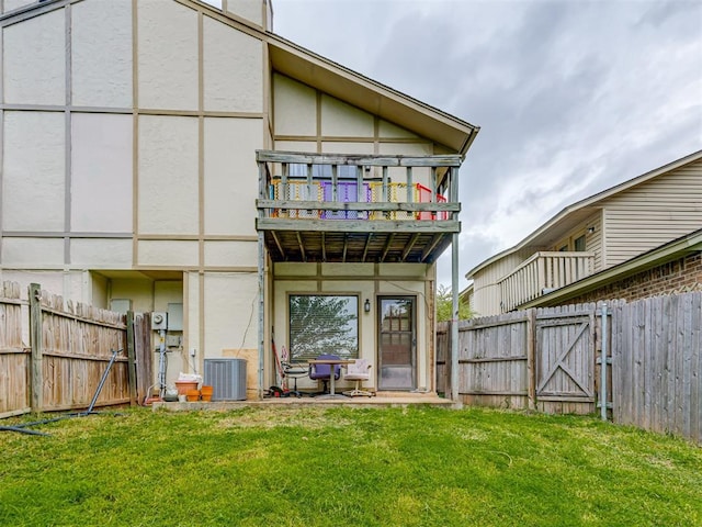 rear view of house with stucco siding, central air condition unit, a lawn, fence, and a balcony