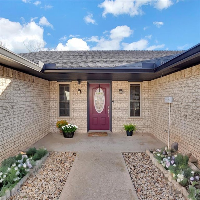 entrance to property featuring brick siding and a shingled roof