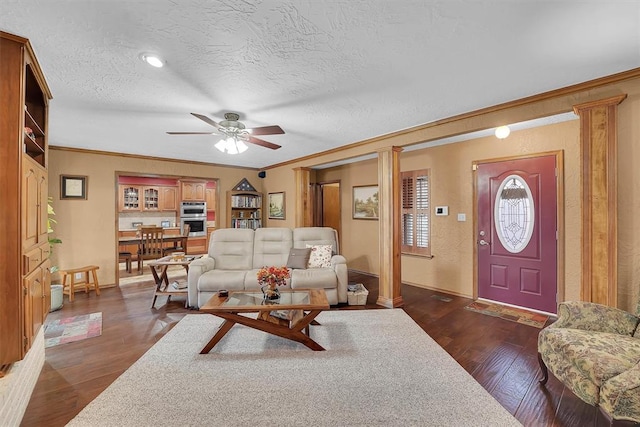 living area with decorative columns, a textured ceiling, dark wood finished floors, and crown molding