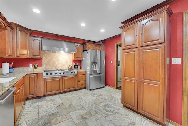 kitchen with light stone counters, tasteful backsplash, stone tile floors, appliances with stainless steel finishes, and wall chimney range hood