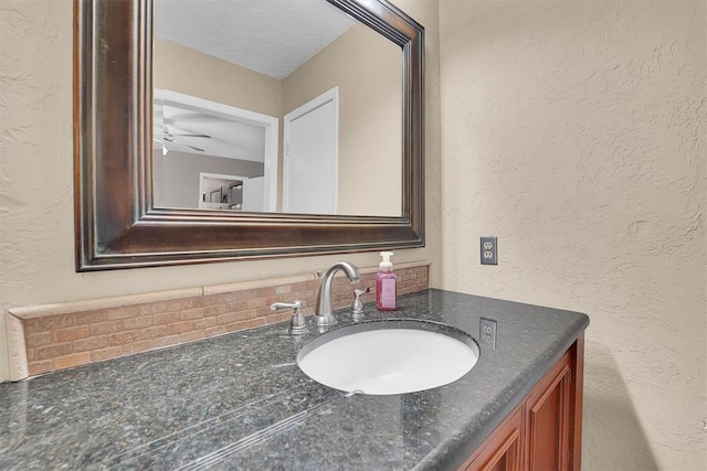 bathroom featuring vanity, ceiling fan, a textured wall, and a textured ceiling