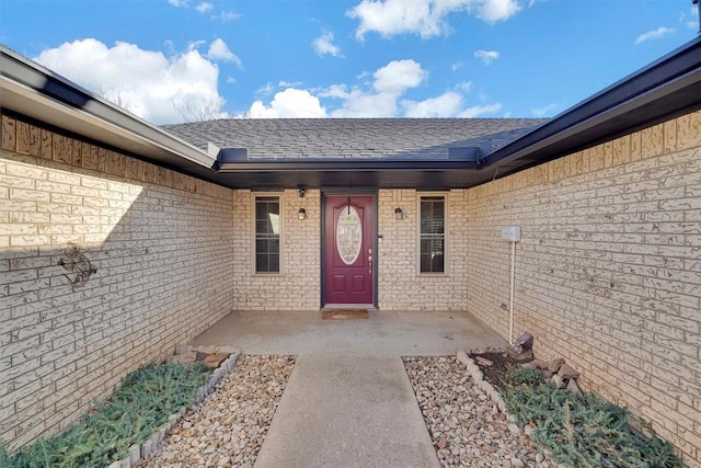 property entrance featuring brick siding and roof with shingles