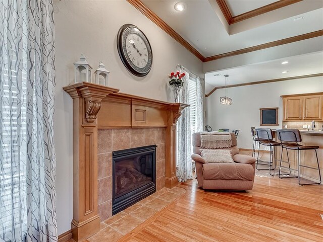 living area with baseboards, recessed lighting, a tiled fireplace, crown molding, and light wood-type flooring