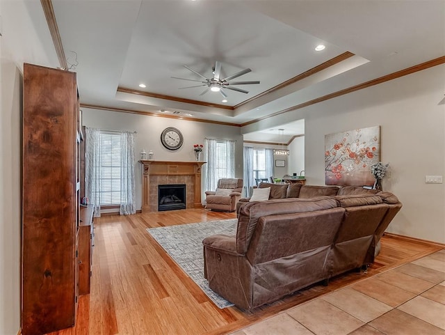 living room featuring a raised ceiling, light wood-style flooring, and a tile fireplace