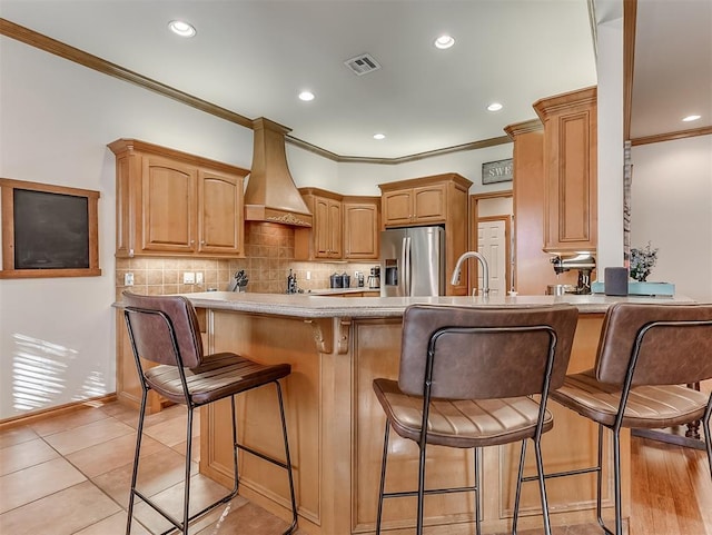 kitchen with visible vents, premium range hood, ornamental molding, a peninsula, and stainless steel refrigerator with ice dispenser