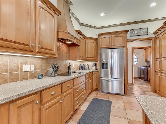 kitchen with premium range hood, washing machine and clothes dryer, stainless steel fridge with ice dispenser, black electric stovetop, and backsplash