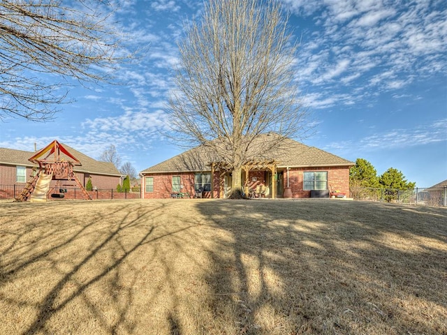 rear view of property with a playground, fence, a lawn, and brick siding