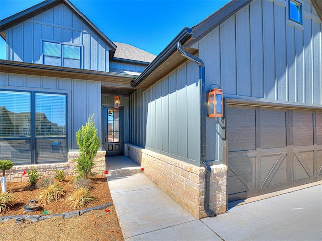 view of exterior entry with a garage, roof with shingles, and board and batten siding