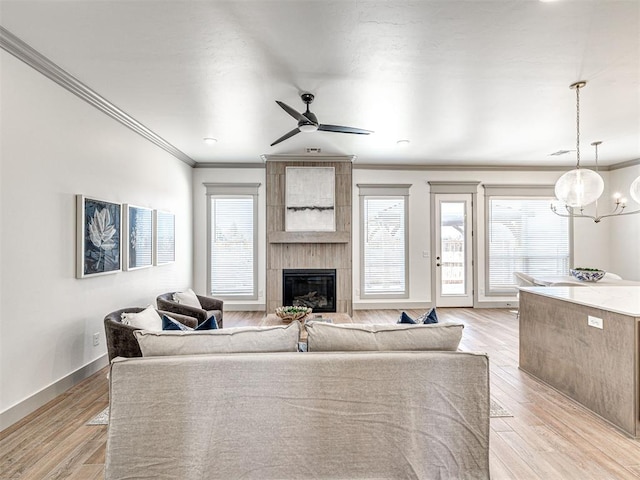 living area with ornamental molding, a ceiling fan, a fireplace, light wood finished floors, and baseboards