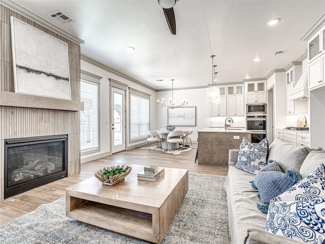 living area featuring a glass covered fireplace, visible vents, ornamental molding, and light wood finished floors