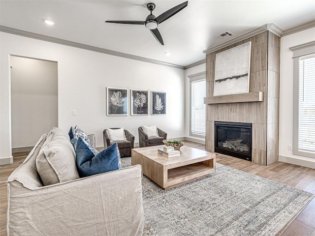 living area featuring visible vents, baseboards, ornamental molding, a fireplace, and wood finished floors