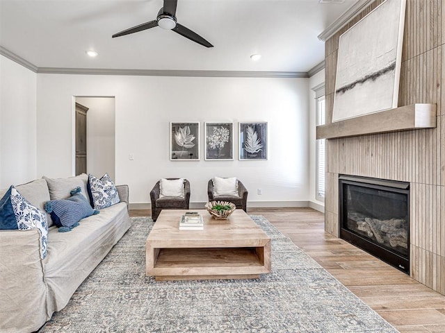 living area with ornamental molding, a ceiling fan, wood finished floors, a large fireplace, and baseboards