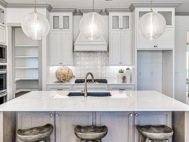 kitchen featuring tasteful backsplash, premium range hood, a center island with sink, stainless steel appliances, and a sink