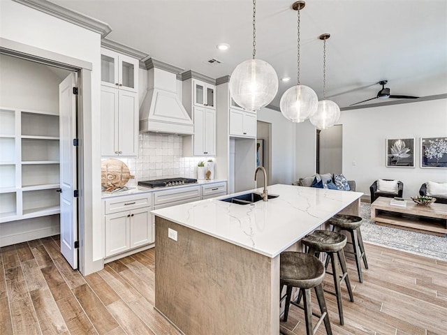 kitchen featuring premium range hood, light wood finished floors, a sink, stainless steel gas stovetop, and open floor plan