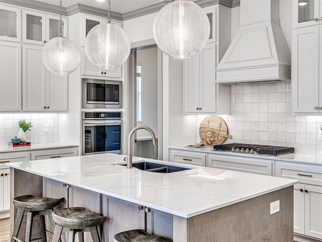 kitchen featuring a kitchen island with sink, a sink, tasteful backsplash, appliances with stainless steel finishes, and custom exhaust hood