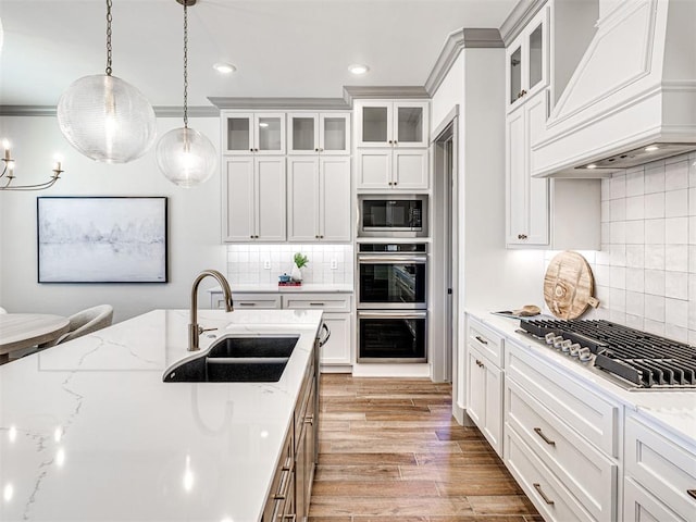 kitchen with premium range hood, light wood finished floors, stainless steel appliances, a sink, and pendant lighting