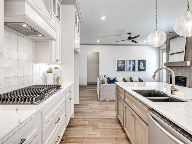 kitchen featuring custom range hood, light stone counters, appliances with stainless steel finishes, light wood-style floors, and a sink