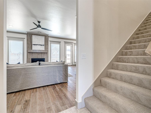 staircase featuring ceiling fan, wood finished floors, a fireplace, and ornamental molding