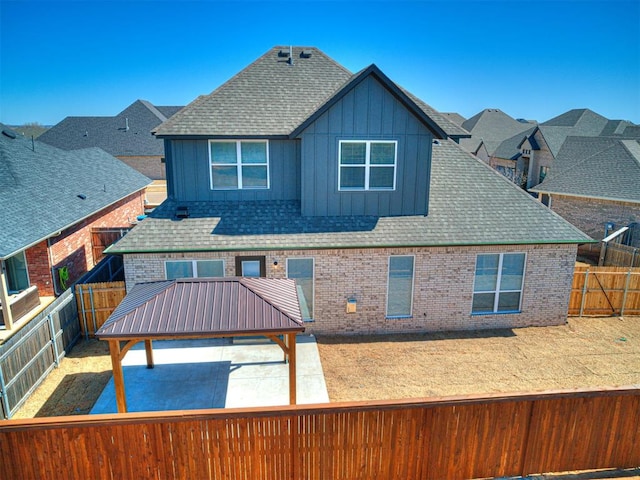 back of property with a gazebo, brick siding, a fenced backyard, and a shingled roof