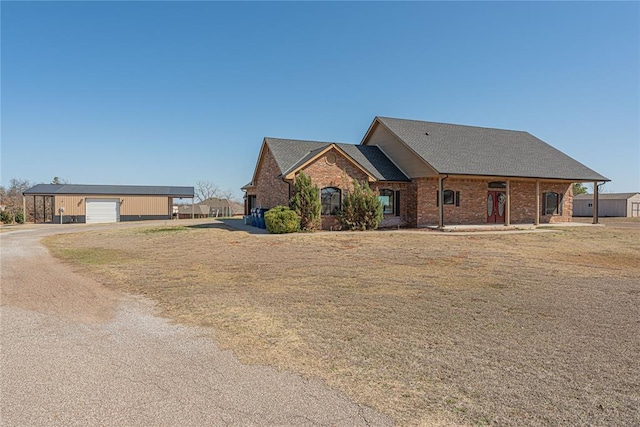 view of front facade featuring dirt driveway, an outdoor structure, a shingled roof, a garage, and brick siding