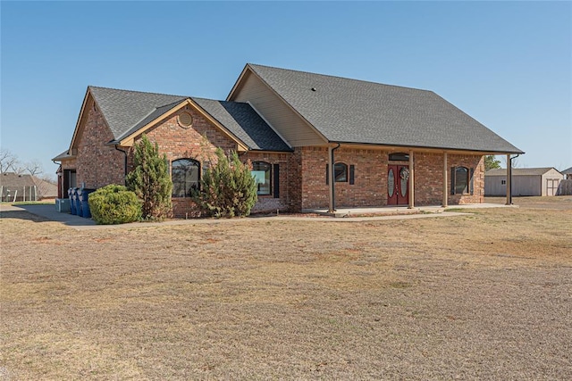 view of front facade featuring brick siding, roof with shingles, and a front yard