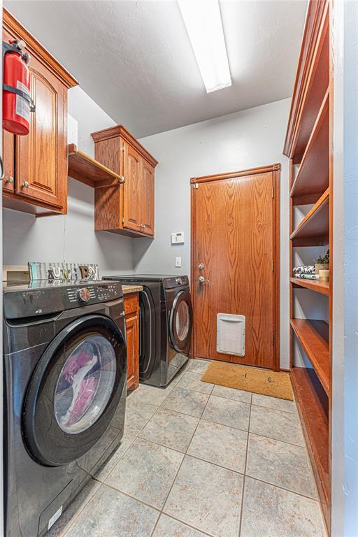 washroom featuring light tile patterned flooring, washing machine and dryer, and cabinet space