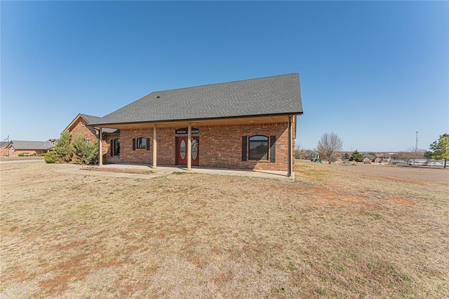 back of house with brick siding, a lawn, and roof with shingles