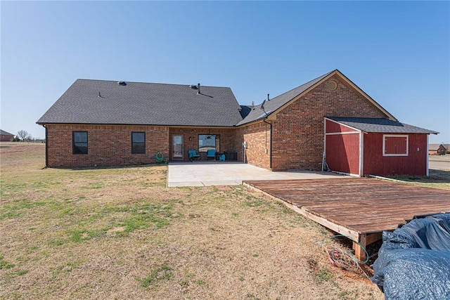 back of property featuring brick siding, a patio area, a lawn, and a shingled roof