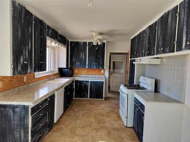 kitchen with white appliances, dark cabinets, under cabinet range hood, and a sink