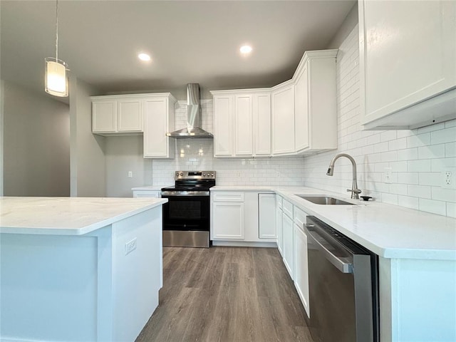 kitchen with appliances with stainless steel finishes, wood finished floors, white cabinetry, wall chimney exhaust hood, and a sink