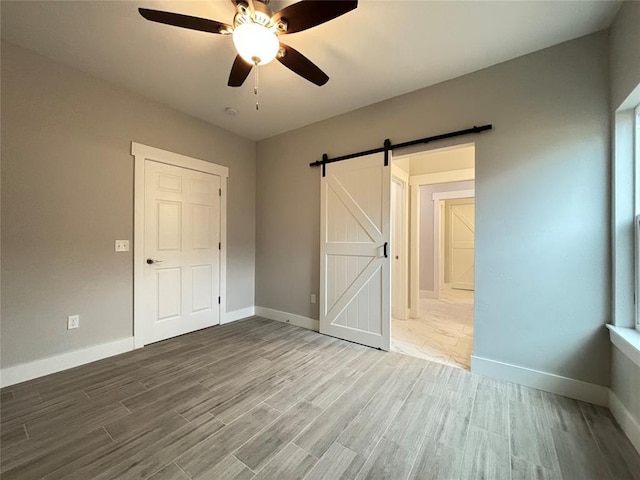 unfurnished bedroom with a ceiling fan, a barn door, wood finished floors, and baseboards