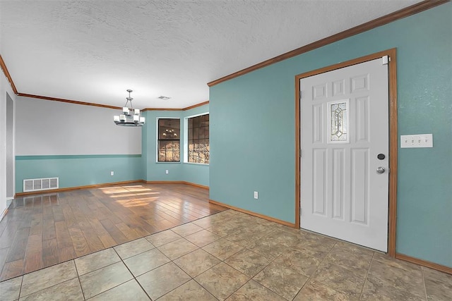 entrance foyer featuring visible vents, a textured ceiling, a chandelier, and crown molding