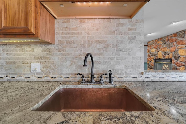 kitchen with backsplash, light stone countertops, wall chimney exhaust hood, and a sink