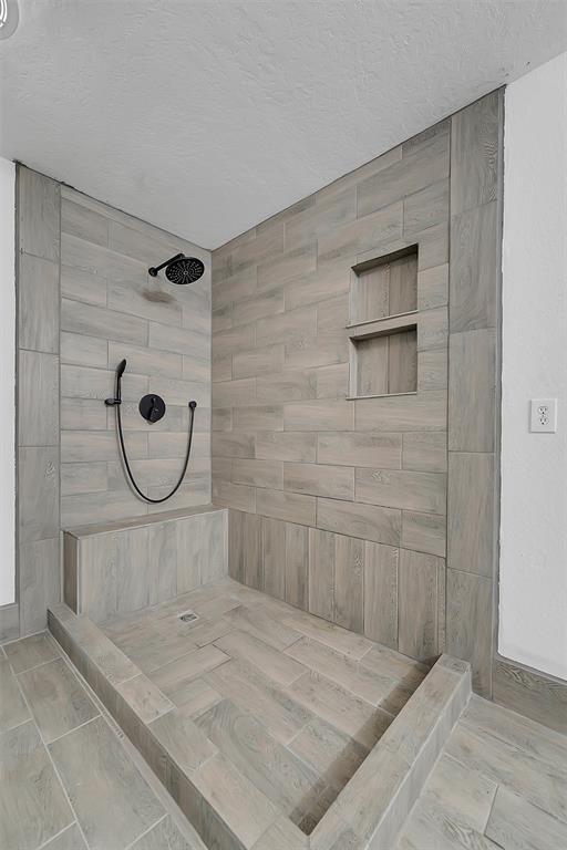 full bathroom with a textured ceiling and tiled shower