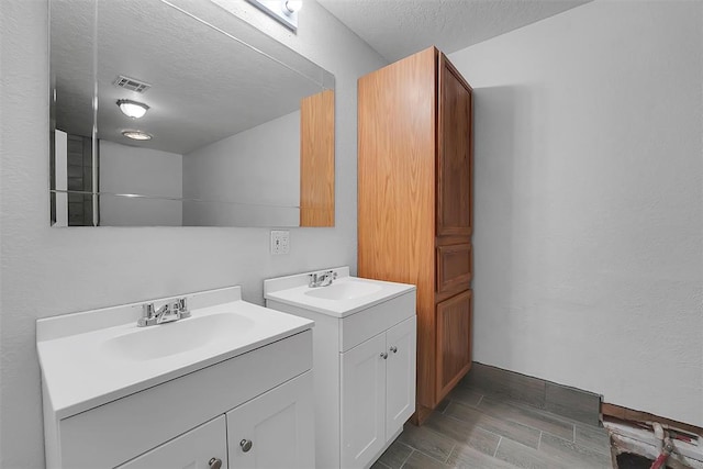 bathroom with a textured ceiling, two vanities, visible vents, and a sink