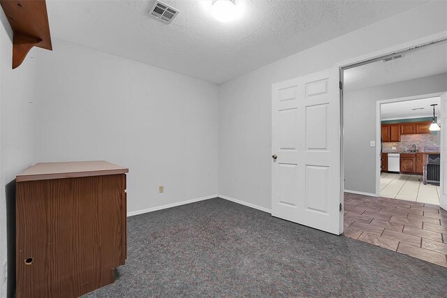 tiled empty room featuring carpet flooring, baseboards, visible vents, and a textured ceiling