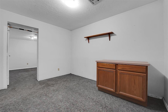 spare room with visible vents, dark carpet, and a textured ceiling