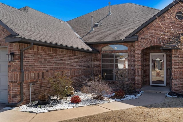 doorway to property featuring brick siding, a garage, and roof with shingles