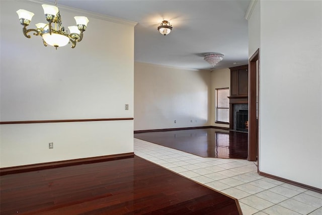 interior space featuring baseboards, light tile patterned flooring, crown molding, a large fireplace, and a chandelier