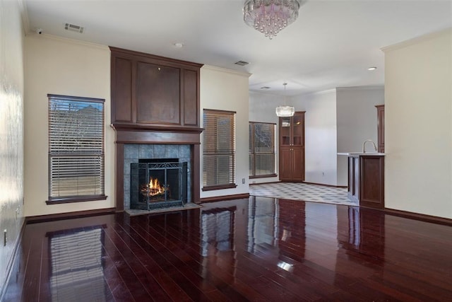 unfurnished living room featuring visible vents, wood finished floors, a tiled fireplace, and ornamental molding