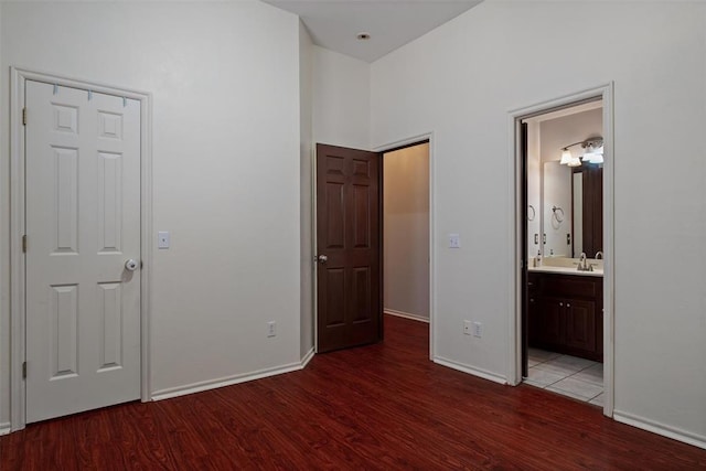 unfurnished bedroom featuring a sink, ensuite bath, baseboards, and wood finished floors